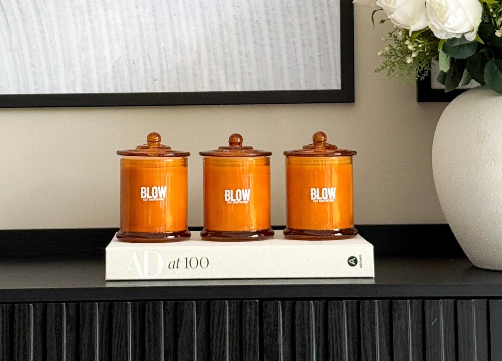 Three orange canisters with wooden lids on a black surface, next to a vase of white flowers.